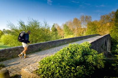 Peregrino con mochila y baston pasando por el puente de la Magdalena en Pamplona